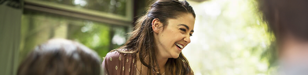 Donna sorridente che tiene una tazza seduta vicino ad un tavolo con un vaso di fiori